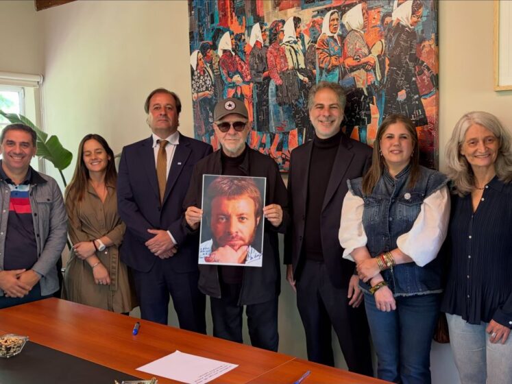 leon gieco recibio el doctorado honoris causa de la universidad nacional del oeste. Foto de la entrega del título, con león sosteniendo un cuadro de él joven que regaló una artista.